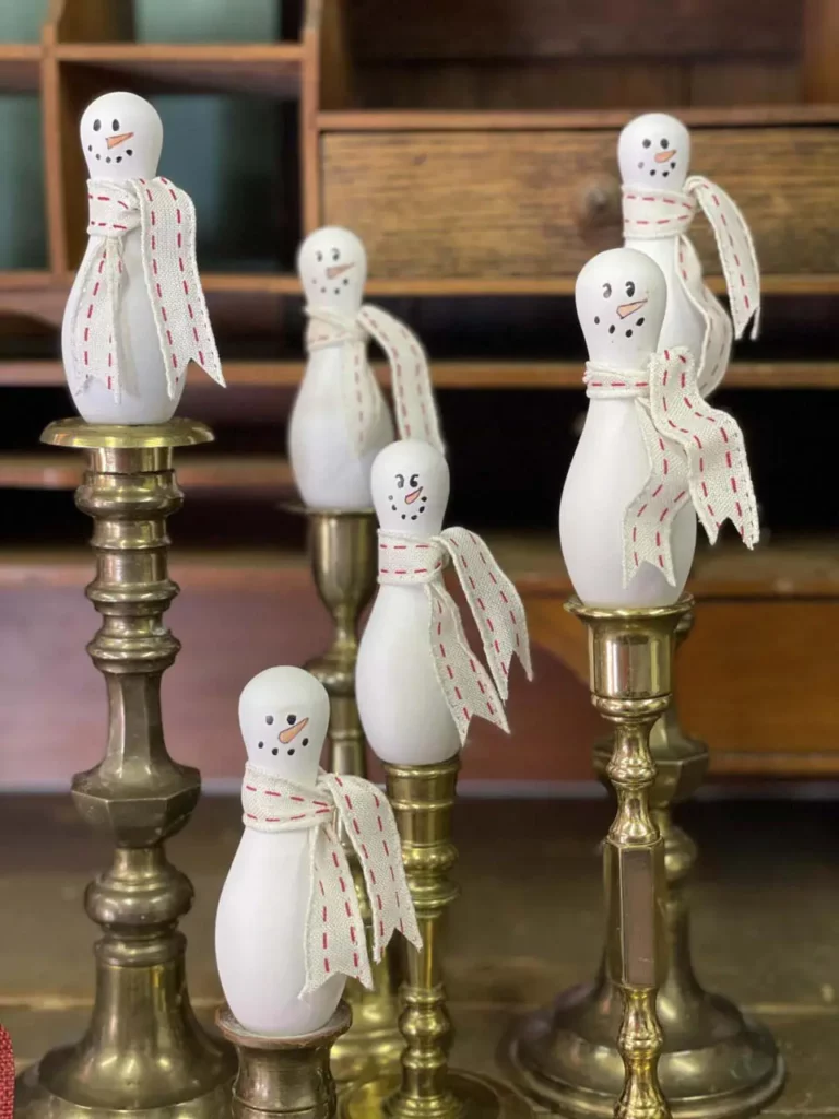 Finished bowling pin snowmen sitting on brass candlesticks.