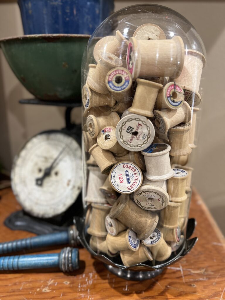 Vintage wooden sewing spools under a glass cloche.