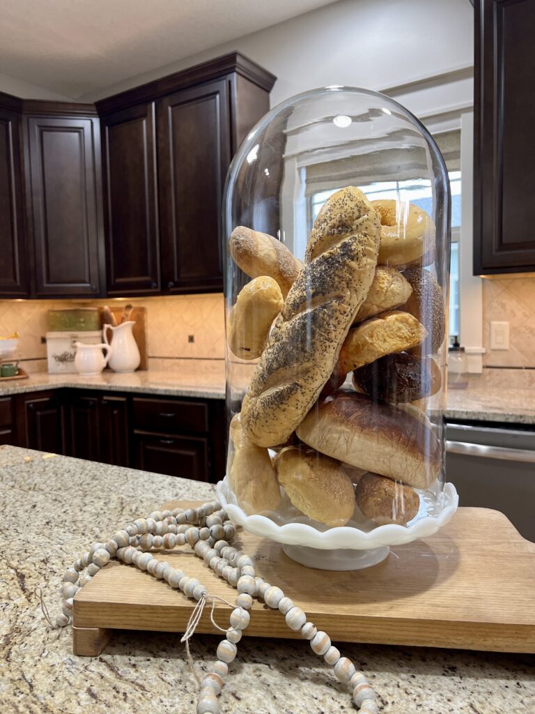 Faux bread in a cloche on a milk glass cake stand on my kitchen island