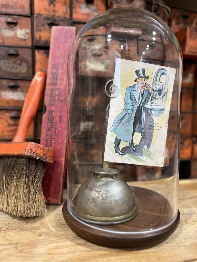 An oil can holding an old post card with a man talking on a phone?  This vignette is displayed under a glass cloche.