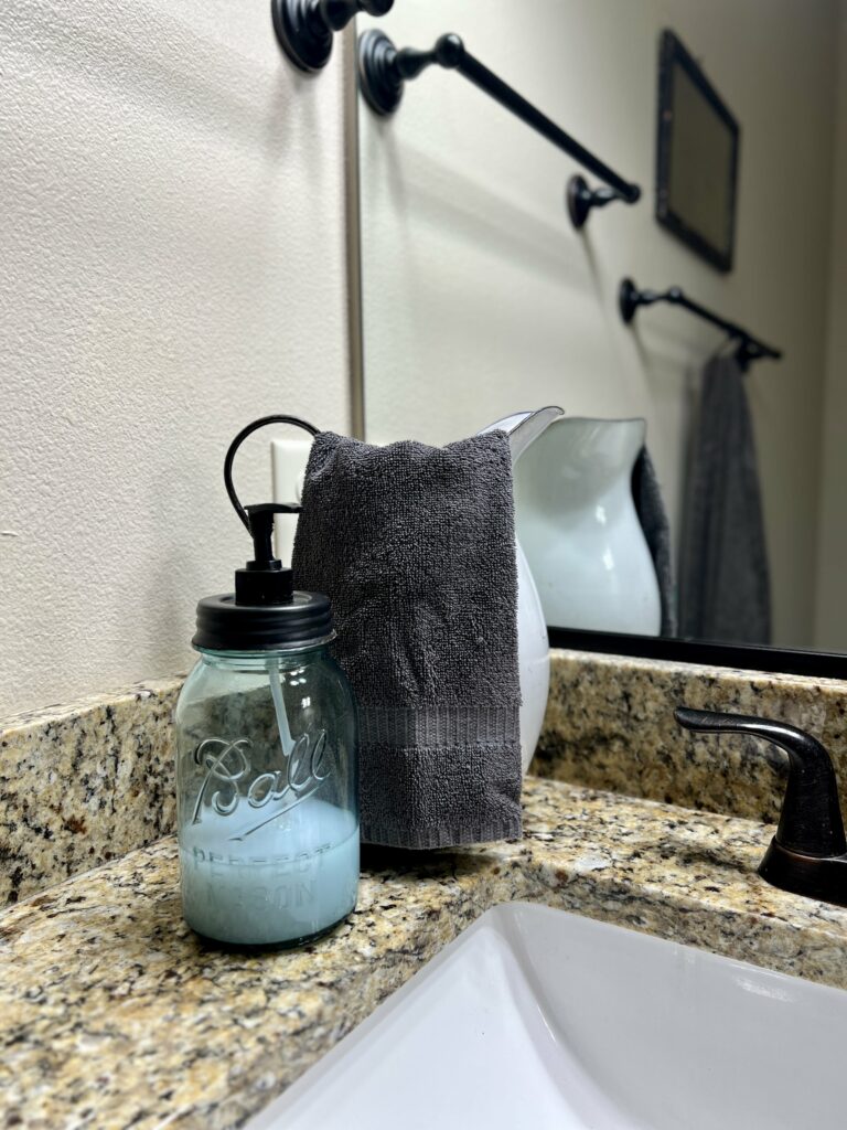 Jar soap dispenser in front of a towel hanging out of an enamel pitcher