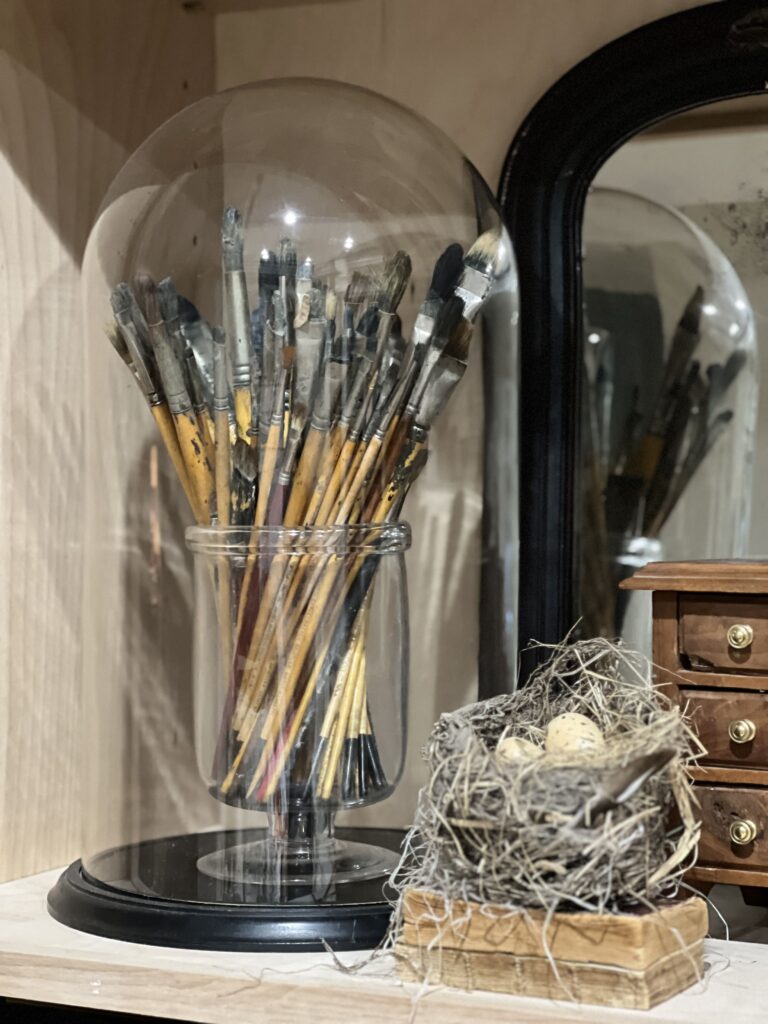 paint brushes under a cloche and nest on book stack
