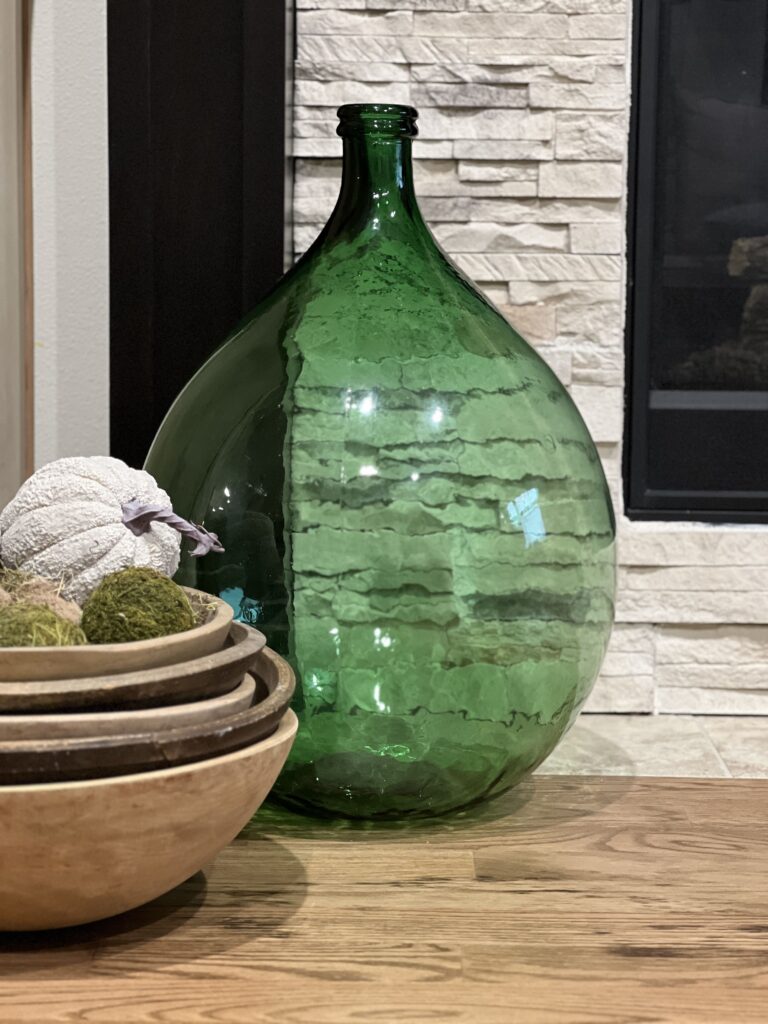 huge green wine jug in front of built ins with wood bowl stack