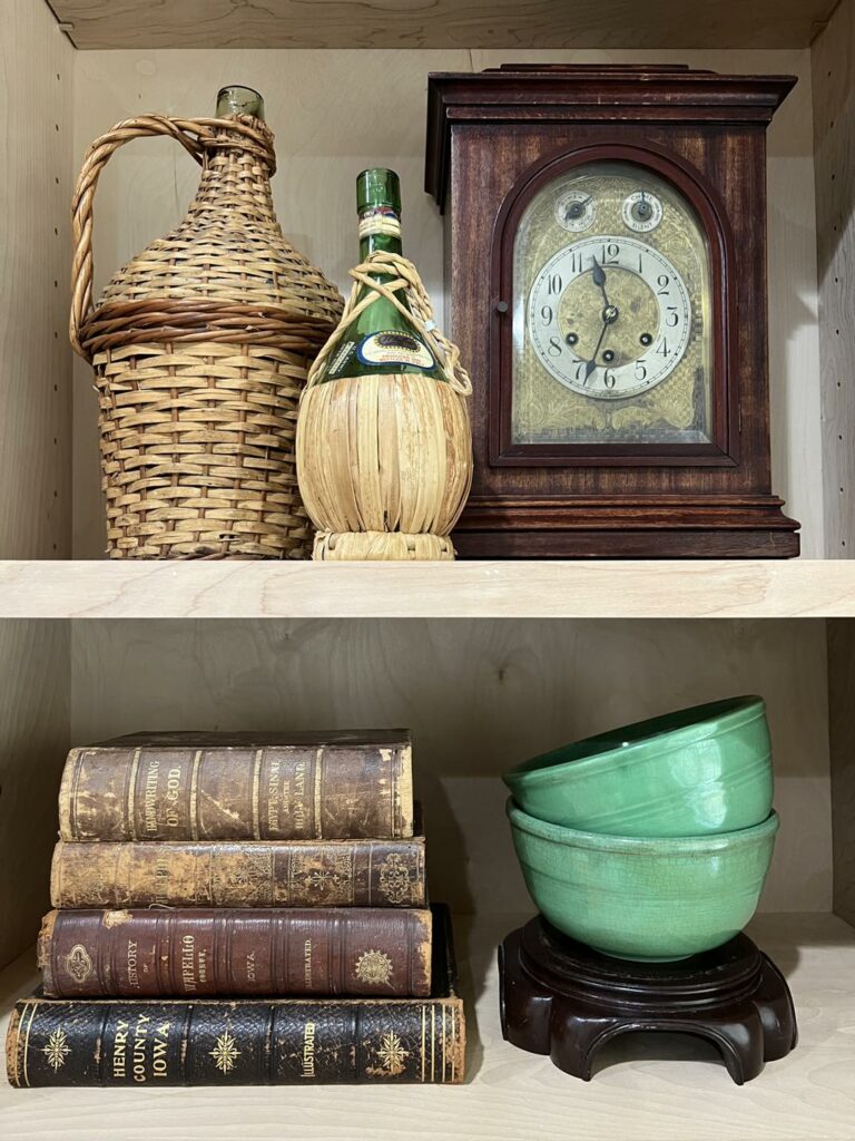 2 sections of built ins. clock with a couple wine jugs and book stack with green bowls