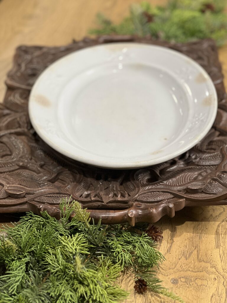 an oval ironstone platter arranged on a wood carved platter with greenery on each side
