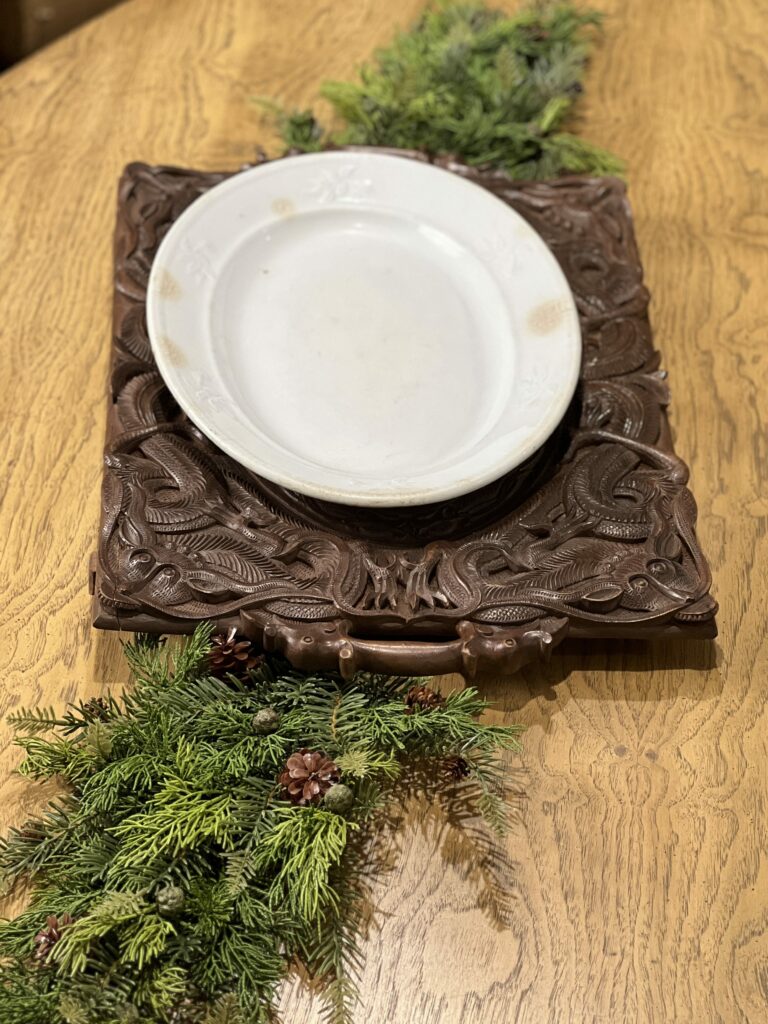 an oval ironstone platter arranged on a wood carved platter with greenery on each side