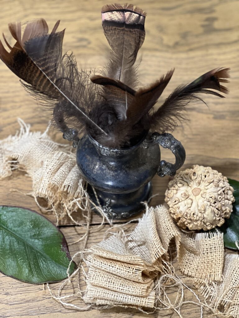 burlap and gourds running down the center of the table with feathers in a silver sugar pot