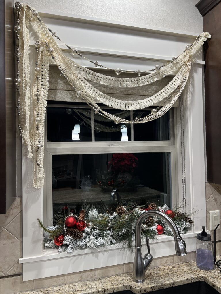 my kitchen window with garland and bulbs and a lace swag curtain