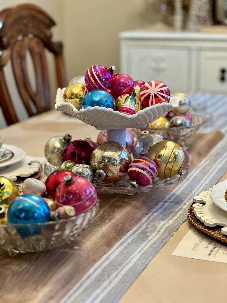 Table centerpiece of compotes, bowls, etc. filled with old ornaments.