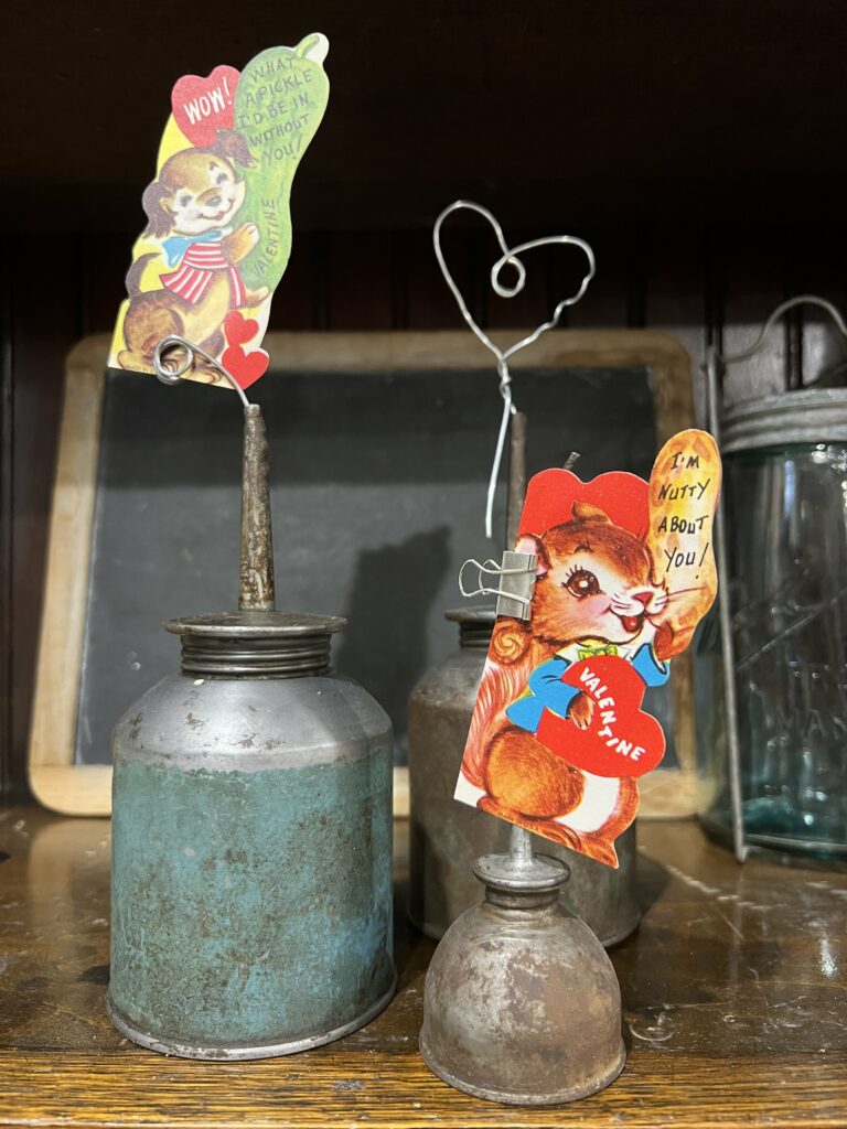 Grouping of oil cans, one with a Valentine clipped to it, one with a wire heart and one with a spiraled wire in the end holding a Valentine